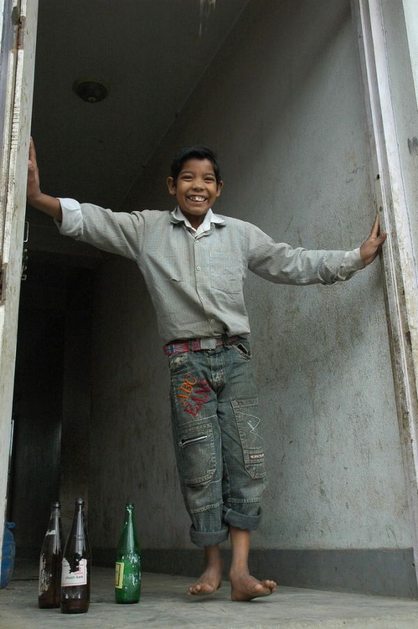 Young man, a boy, saying hello with a broad smile from the doorway of a house, bottles, Boudha, Kathmandu, Nepal